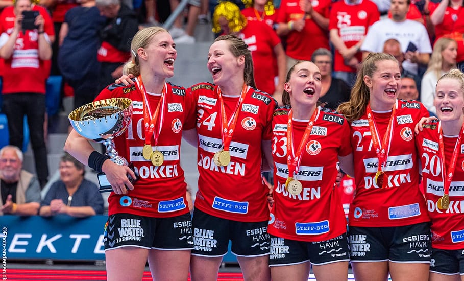 Team Esbjerg genvandt mesterskabet i 2022/2023 og her ses tre glade spillere, hvor Kathrine Heindahl, Sanne Solberg og Julie Bøe Jacobsen jubler med pokalen i Blue Water Dokken
